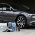 A dark sedan parked next to organized car washing supplies on a concrete floor.