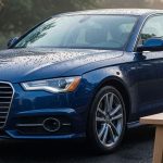 A spotless dark blue sedan in a shaded driveway with fresh water droplets.