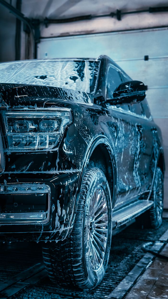 Close-up of a sleek SUV covered in soap during a car wash, highlighting cleanliness and care.