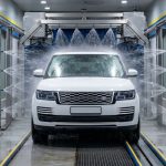 A white SUV passes through a modern car wash with water spraying around it.