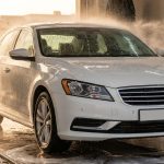 White sedan being cleaned by water jets and foam inside an automatic car wash.