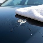A white towel removes bird droppings from a glossy car hood.