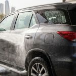 A dark SUV is rinsed at a sunny Abu Dhabi car wash beneath a red headline band.