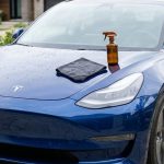 Spotless car with a microfiber cloth and spray bottle on a natural driveway.