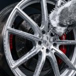 A silver alloy wheel is gently cleaned with a foaming microfiber mitt.