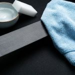 Gray seat belt being wiped with a microfiber cloth beside soapy water.
