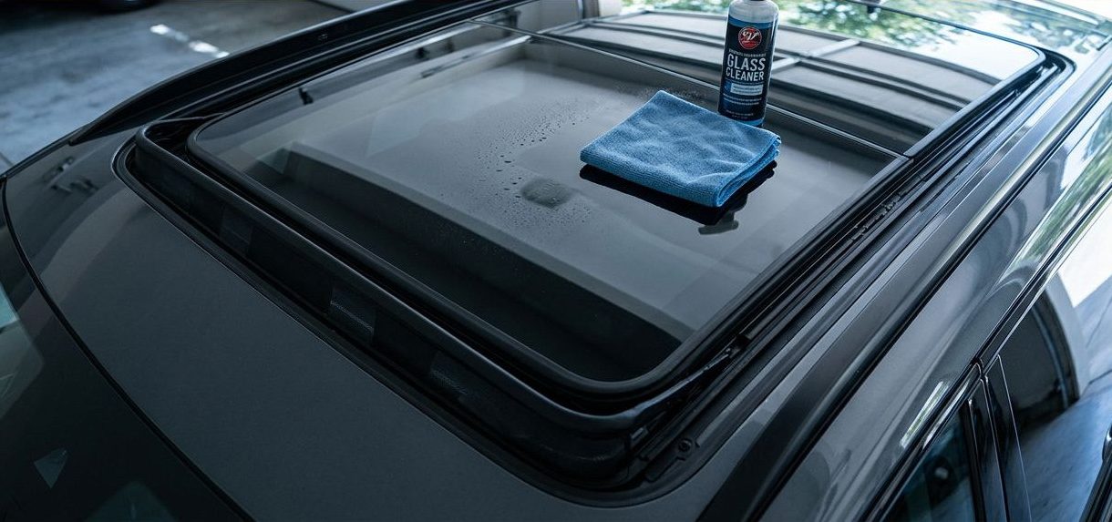 Car sunroof with a microfiber cloth, glass cleaner, rubber seal, and drainage edge.