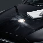 Black car hood with swirl marks, an inspection light, microfiber towel, and detailing mitt.