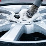 A brush and foam remove brake dust from a silver alloy wheel.