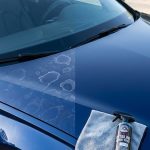Dark blue car showing water spots beside a towel and detailing spray.