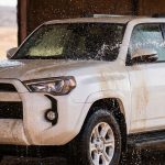 Water rinses a dusty white SUV in a desert setting.