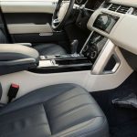 Vacuum nozzle cleaning a spotless car carpet beside leather seats and a visible dashboard touchscreen.
