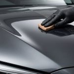 Gloved hand using a clay bar on a car bonnet with clean and gritty paint sections.