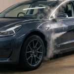 Technician steams a dark sedan’s front door in a clean detailing bay.