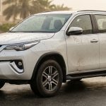 White SUV covered in muddy spots on a wet Dubai street.