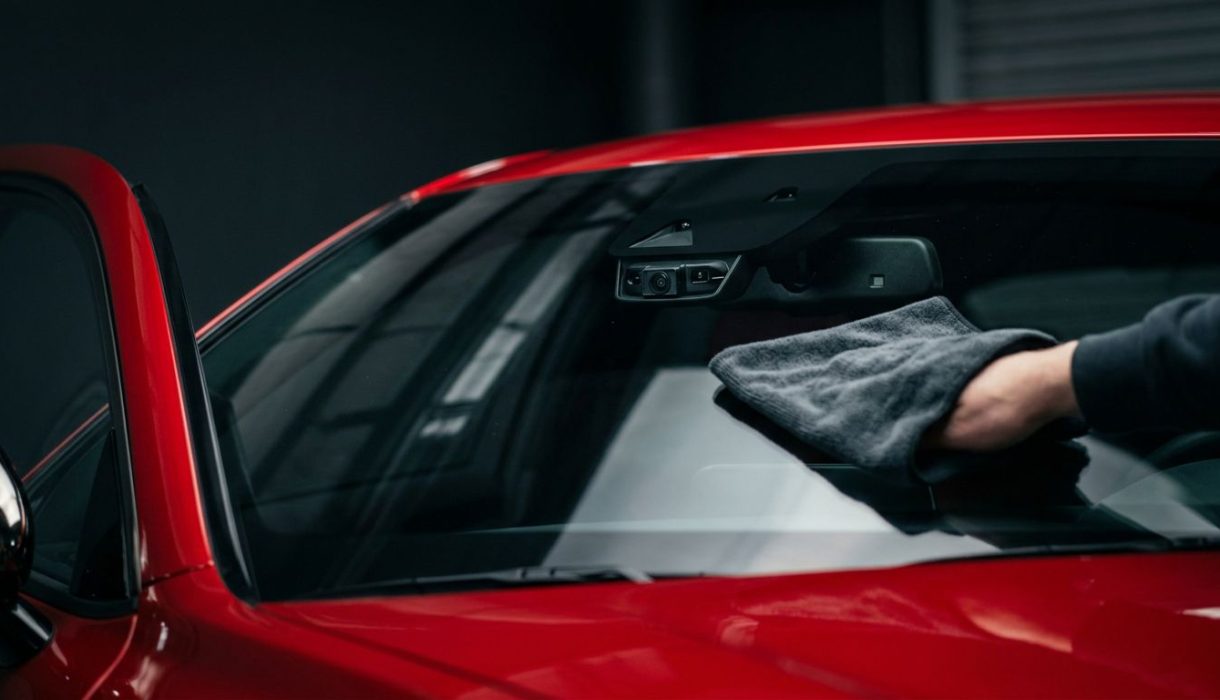 A microfiber cloth cleans the windshield near a red car’s ADAS camera.