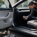 A technician inspects a car interior beside neatly arranged personal items.